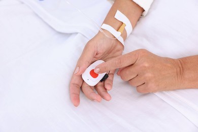 Senior woman pressing emergency call button on bed, top view