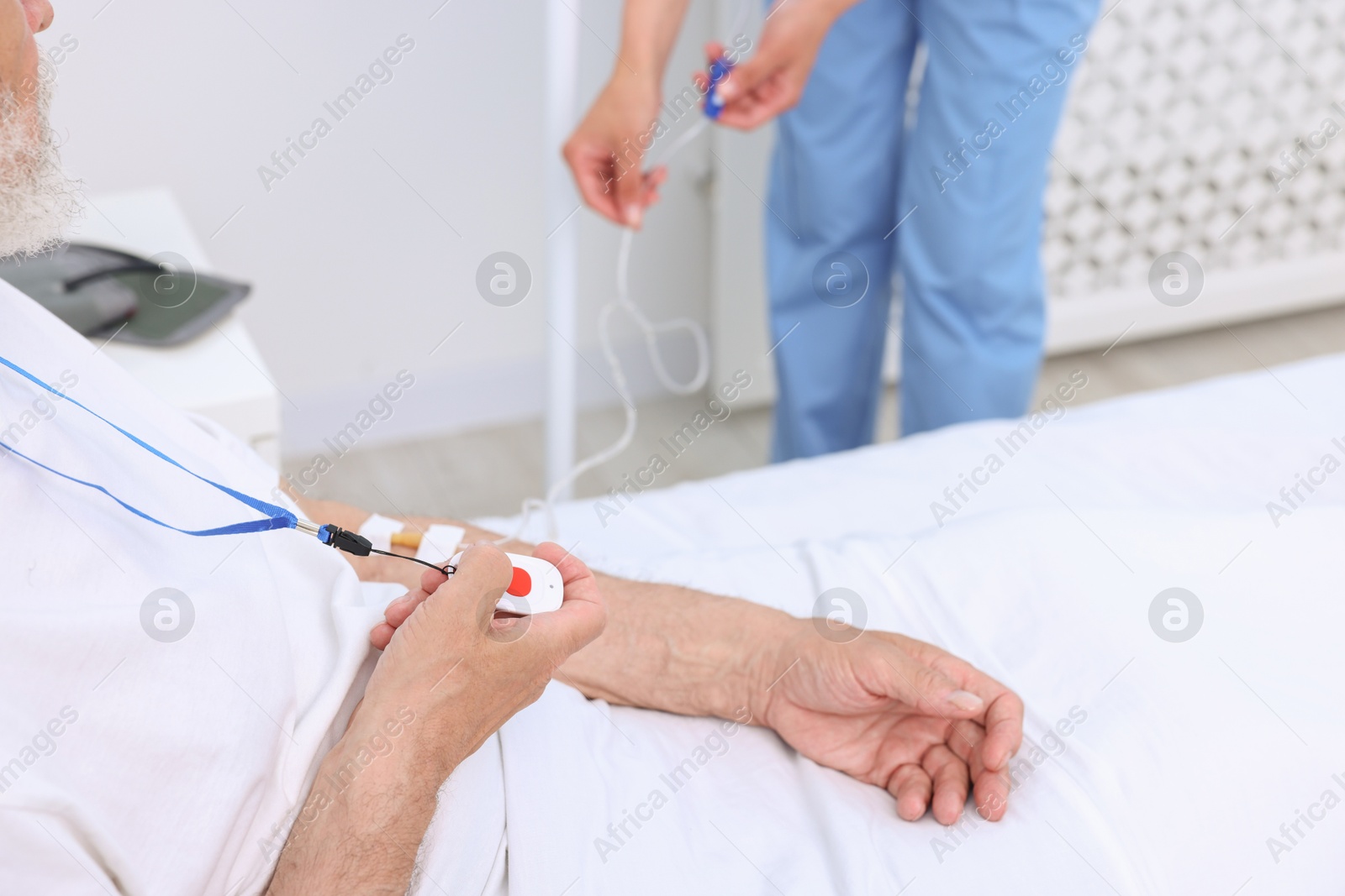 Photo of Senior man with emergency call button and nurse setting IV drip in hospital, closeup