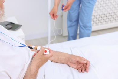 Photo of Senior man with emergency call button and nurse setting IV drip in hospital, closeup