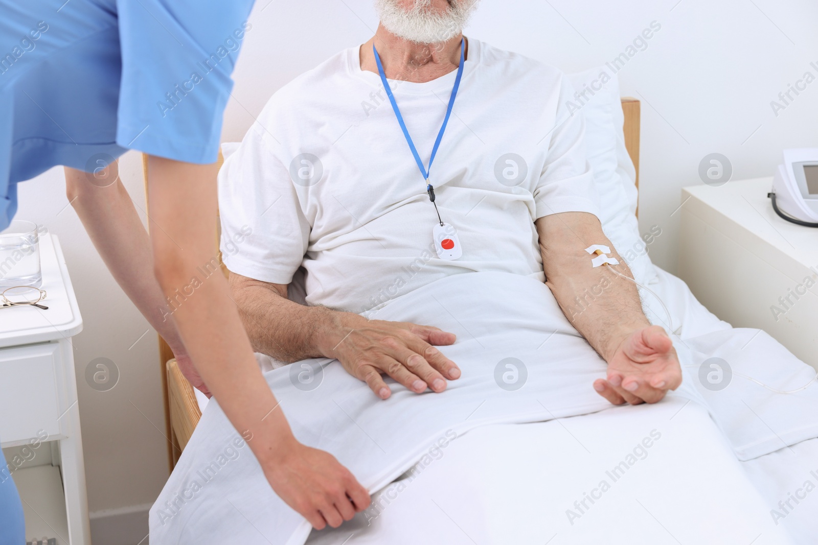 Photo of Nurse making patient's bed in a hospital, closeup. Senior man with emergency call button indoors