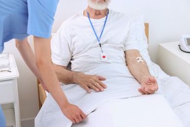 Nurse making patient's bed in a hospital, closeup. Senior man with emergency call button indoors