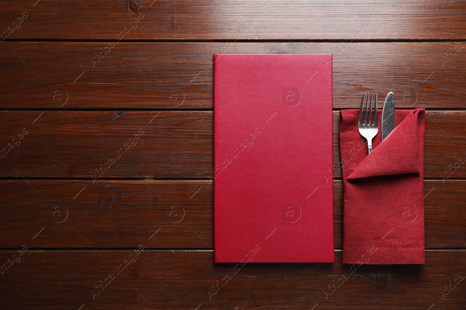 Photo of Hardcover menu and cutlery on wooden table, flat lay. Space for text