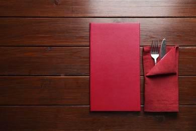 Photo of Hardcover menu and cutlery on wooden table, flat lay. Space for text