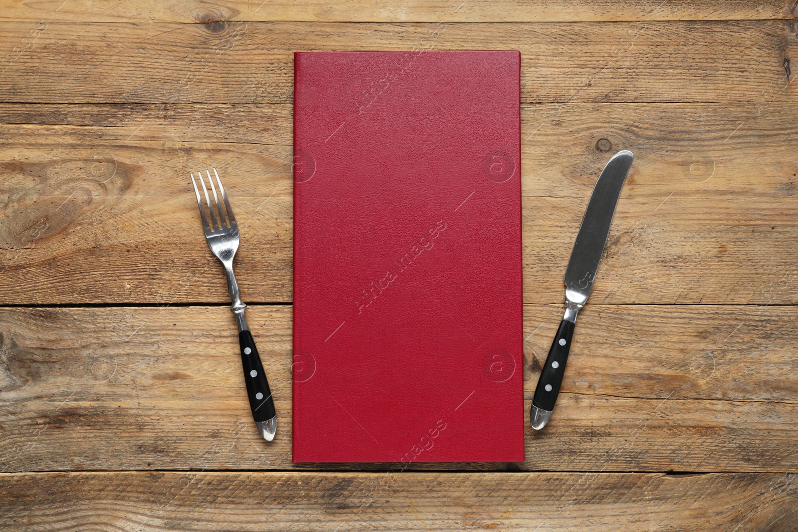 Photo of Hardcover menu and cutlery on wooden table, flat lay