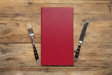 Photo of Hardcover menu and cutlery on wooden table, flat lay