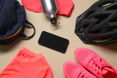 Photo of Bicycle helmet, sportswear, smartphone with blank screen and bottle on beige background, flat lay