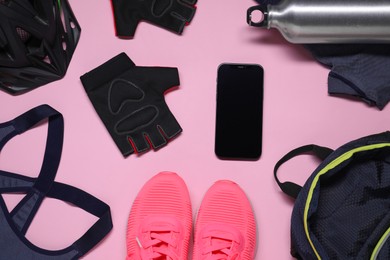 Bicycle helmet, sportswear, sneakers, thermo bottle and smartphone on pink background, flat lay