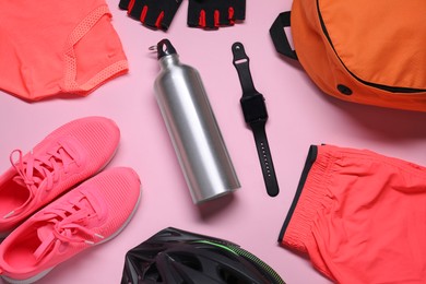 Bicycle helmet, sportswear, sneakers, thermo bottle and wristwatch on pink background, flat lay