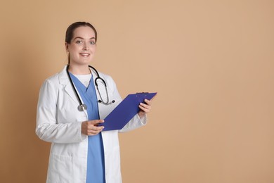 Portrait of professional nurse with clipboard on dark beige background. Space for text