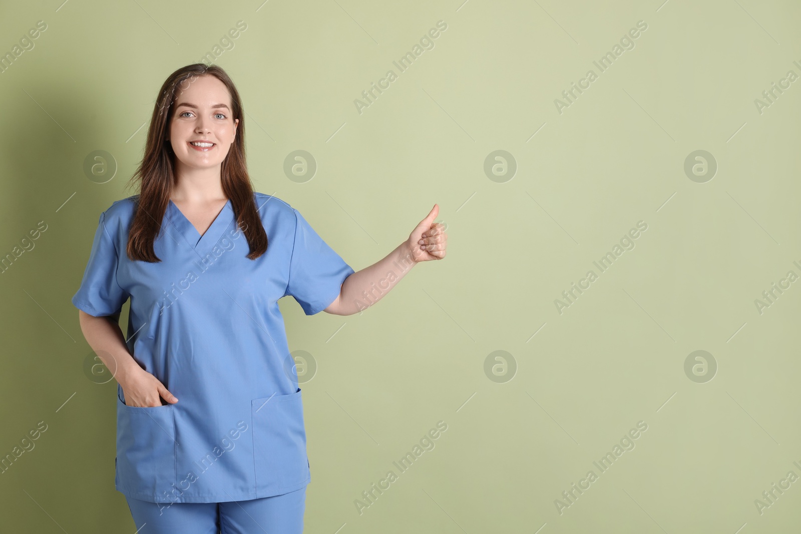 Photo of Professional nurse in uniform showing thumbs up on pale green background. Space for text