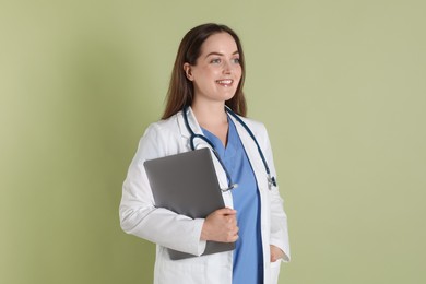 Professional nurse with laptop and stethoscope on pale green background