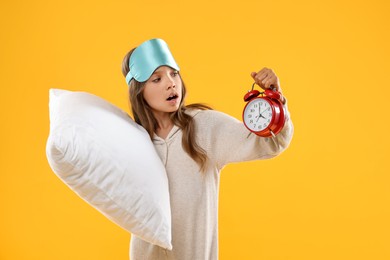 Photo of Overslept girl with sleep mask, pillow and alarm clock on orange background