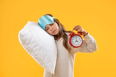 Photo of Overslept girl with sleep mask, pillow and alarm clock on orange background