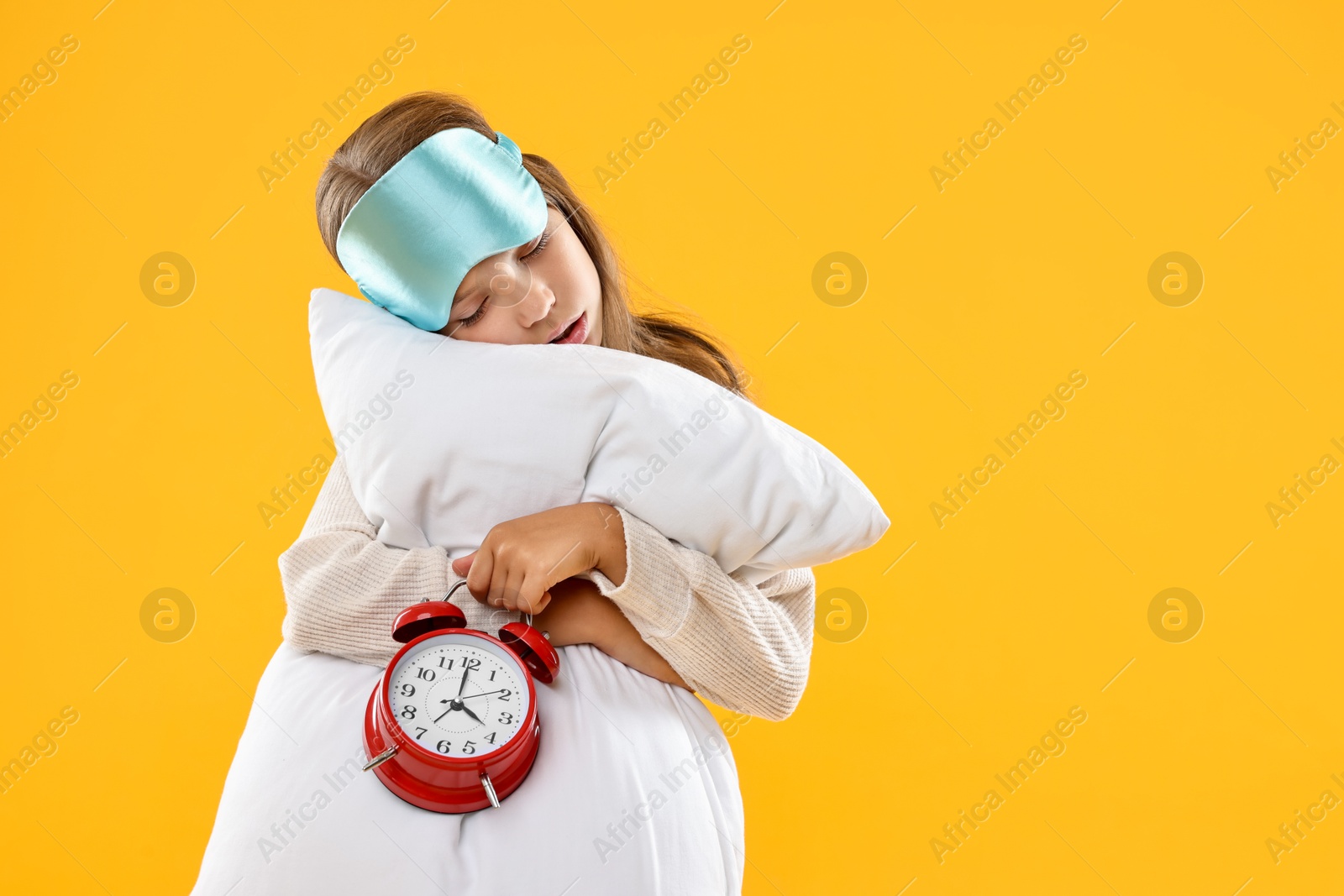 Photo of Overslept girl with sleep mask, pillow and alarm clock on orange background, space for text