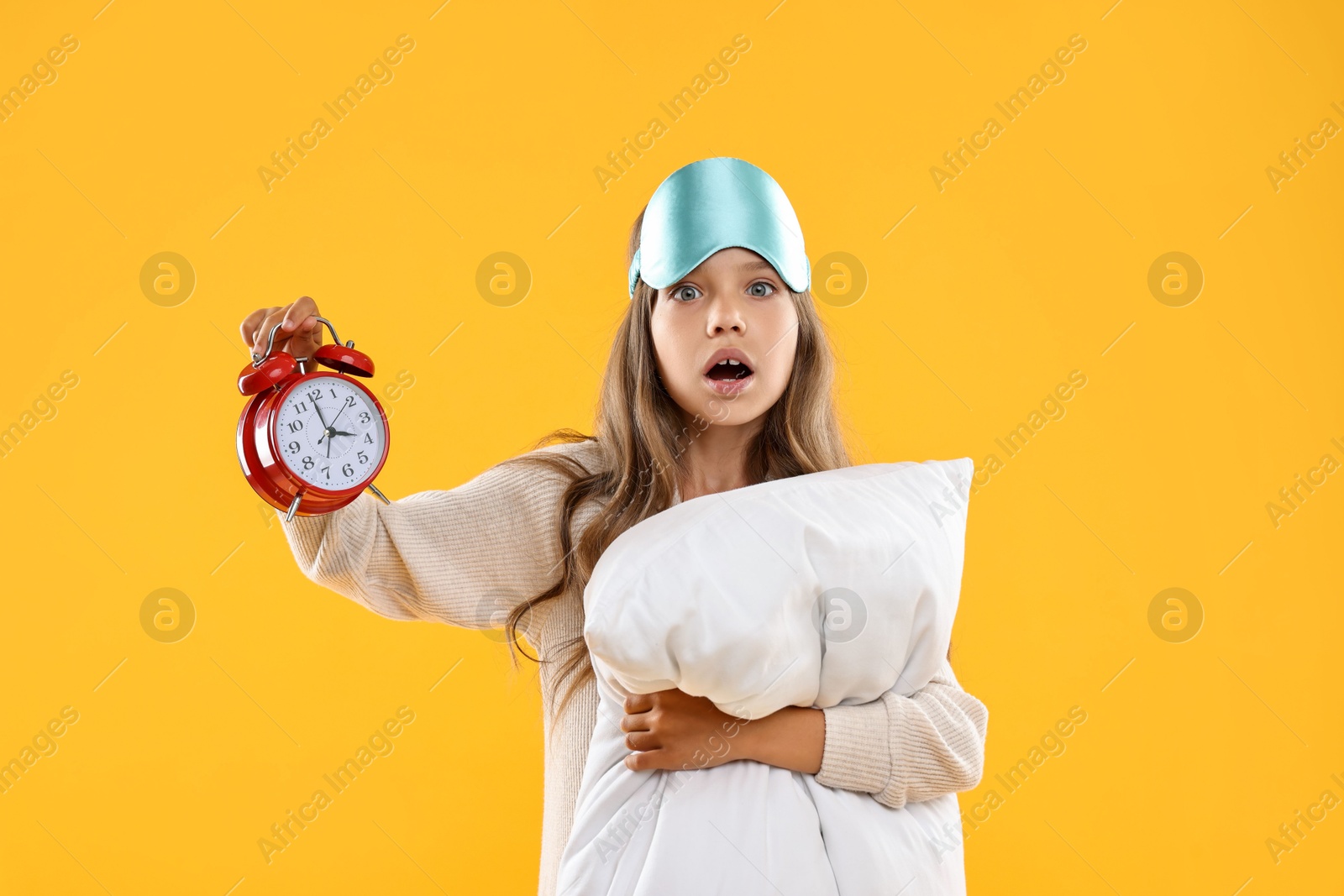 Photo of Overslept girl with sleep mask, pillow and alarm clock on orange background