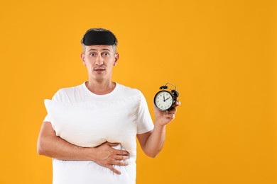 Photo of Overslept man with sleep mask, pillow and alarm clock on orange background, space for text