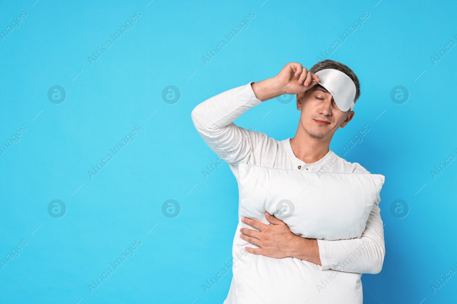 Photo of Overslept man with sleep mask and pillow on light blue background, space for text