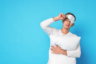 Overslept man with sleep mask and pillow on light blue background, space for text