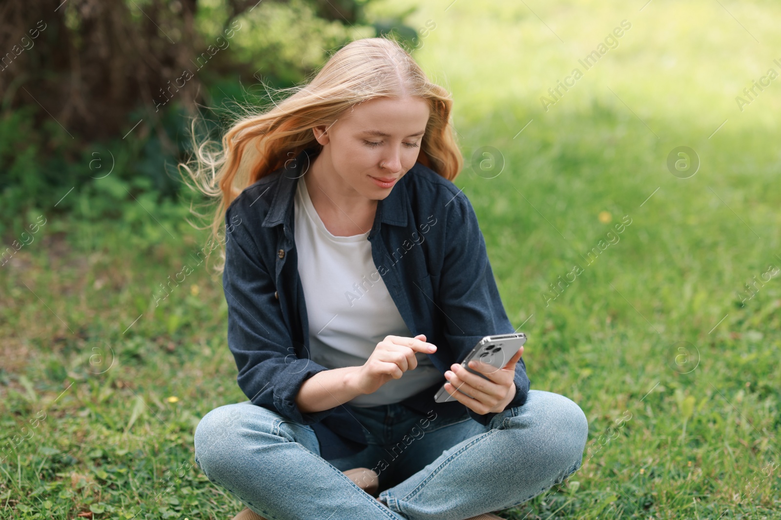 Photo of Beautiful woman using smartphone on green grass outdoors