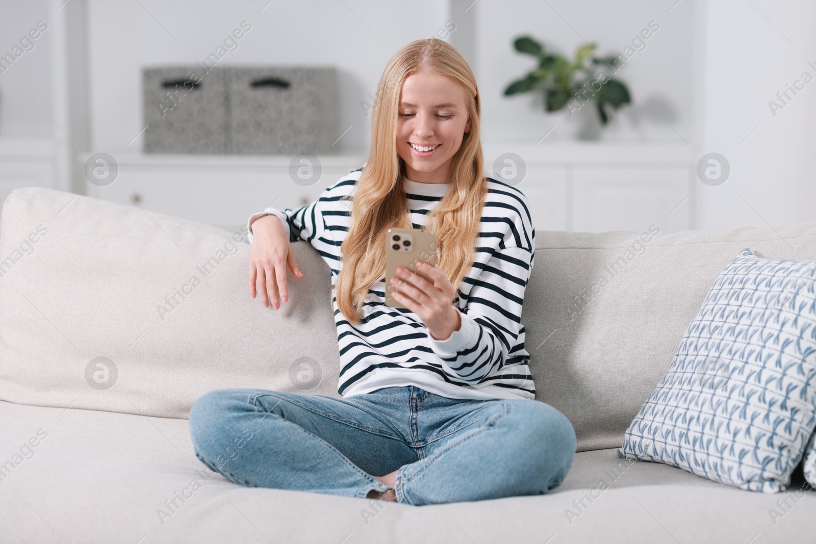 Photo of Smiling woman using smartphone on sofa indoors