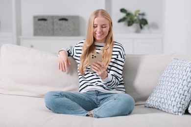 Smiling woman using smartphone on sofa indoors