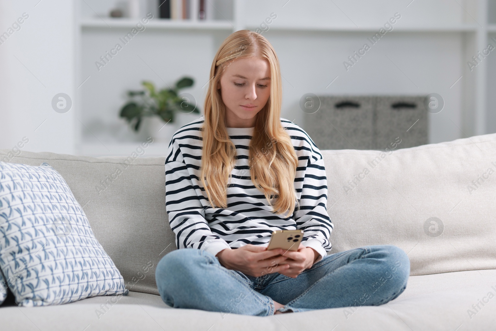 Photo of Beautiful woman using smartphone on sofa indoors