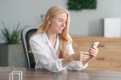 Smiling woman using smartphone and drinking coffee at table in office