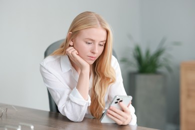 Beautiful woman using smartphone at table in office