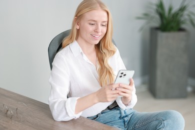 Photo of Smiling woman using smartphone at table in office