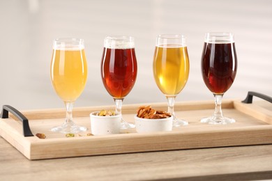 Photo of Glasses with different types of beer and snacks on wooden table indoors