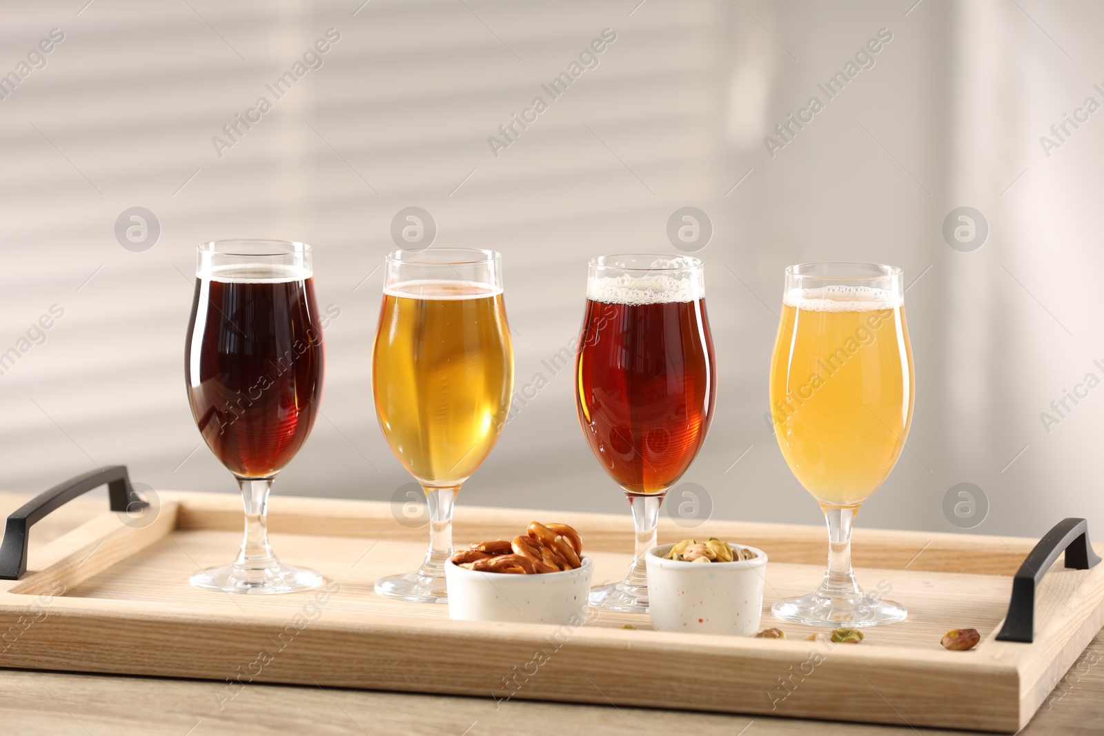 Photo of Glasses with different types of beer and snacks on wooden table indoors