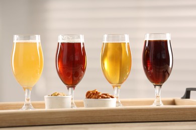 Photo of Glasses with different types of beer and snacks on wooden table indoors