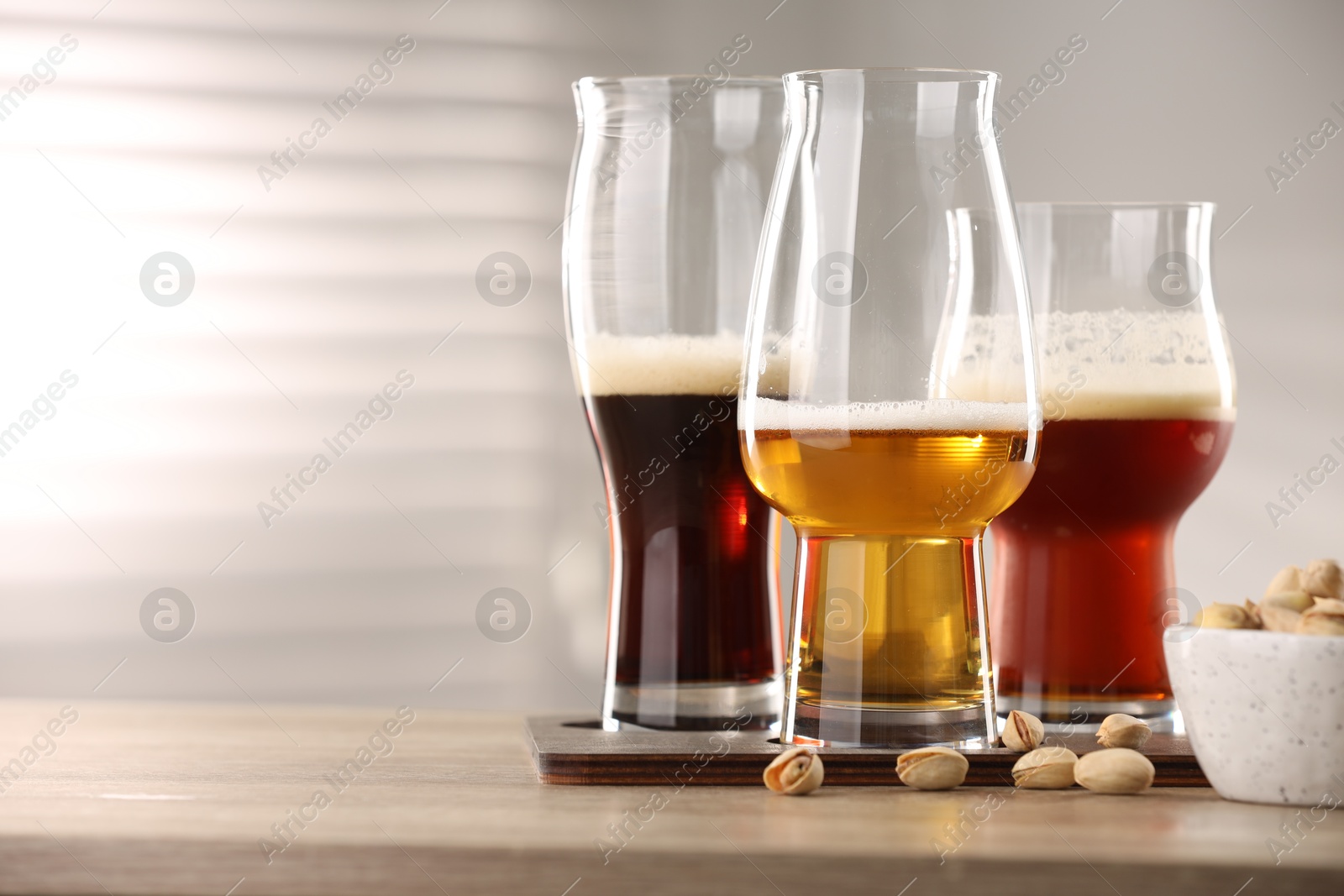 Photo of Glasses with different types of beer and pistachio nuts on wooden table indoors, space for text