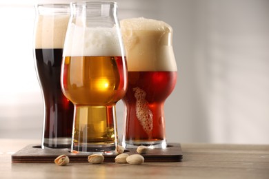 Photo of Glasses with different types of beer and pistachio nuts on wooden table indoors, closeup. Space for text