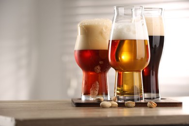 Photo of Glasses with different types of beer and pistachio nuts on wooden table indoors, closeup. Space for text