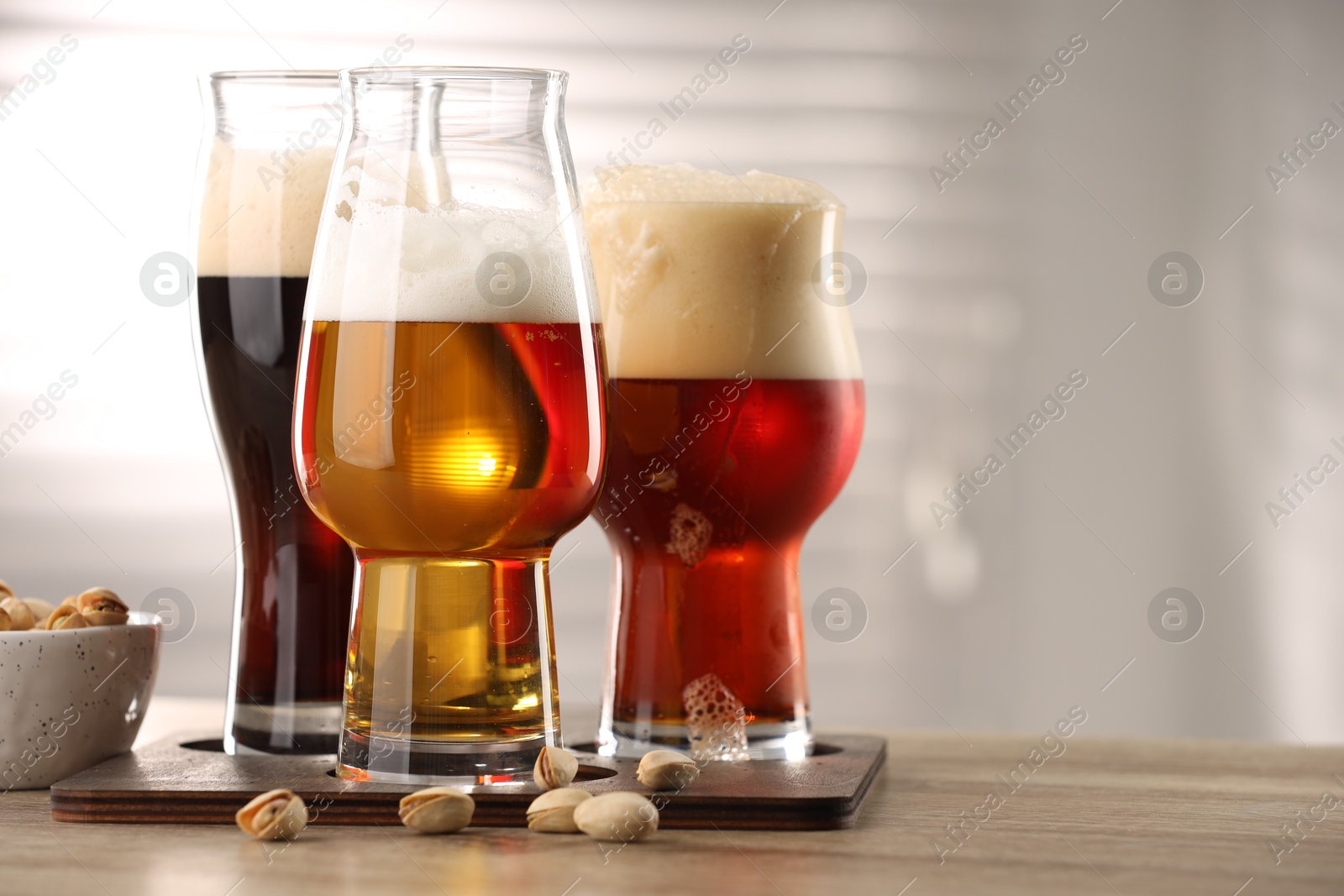 Photo of Glasses with different types of beer and pistachio nuts on wooden table indoors, closeup. Space for text