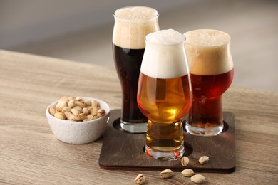 Photo of Glasses with different types of beer and pistachio nuts on wooden table indoors