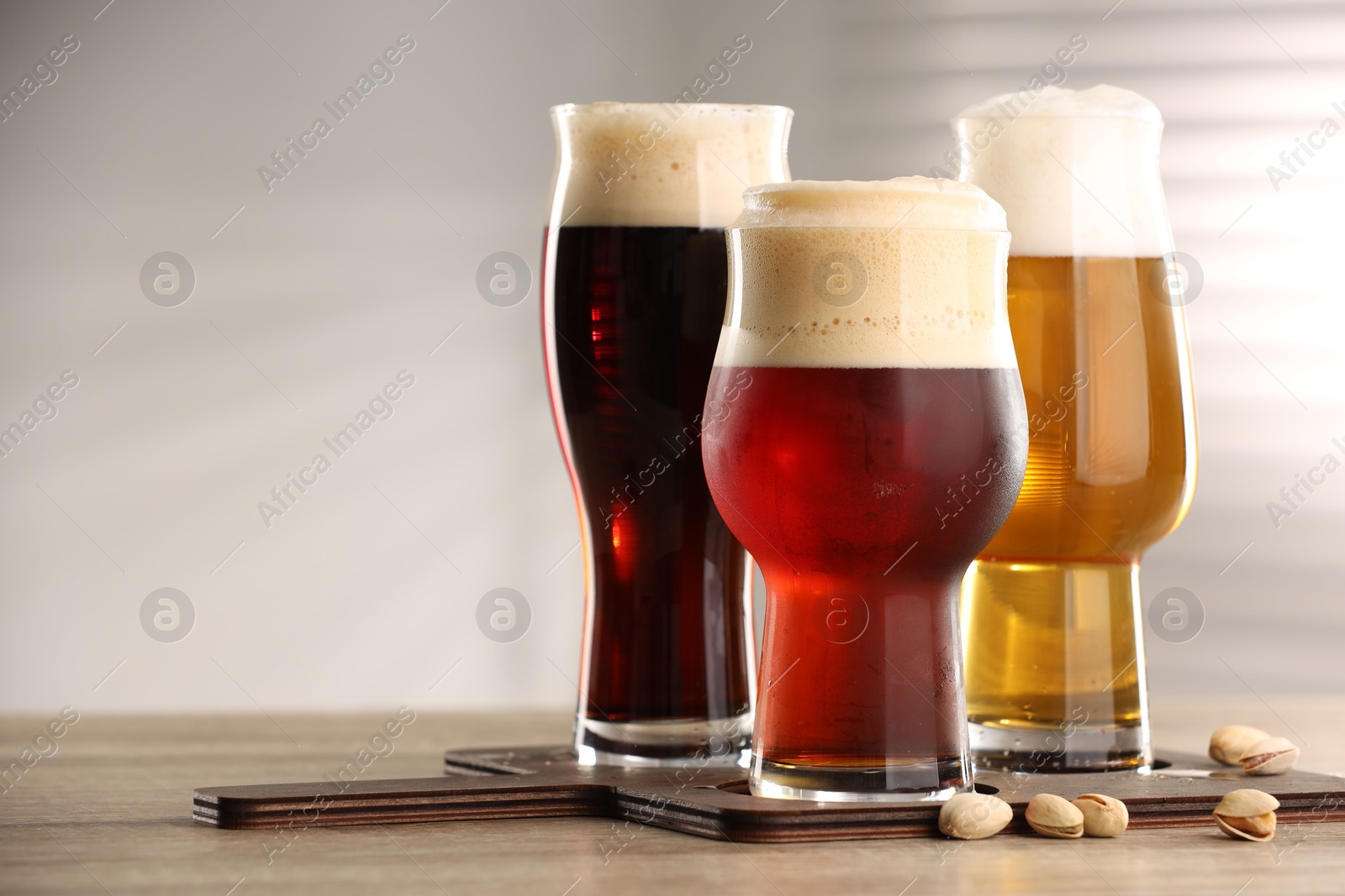 Photo of Glasses with different types of beer and pistachio nuts on wooden table indoors, space for text