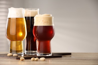 Photo of Glasses with different types of beer and pistachio nuts on wooden table indoors, space for text