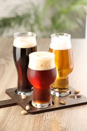 Photo of Glasses with different types of beer and pistachio nuts on wooden table indoors