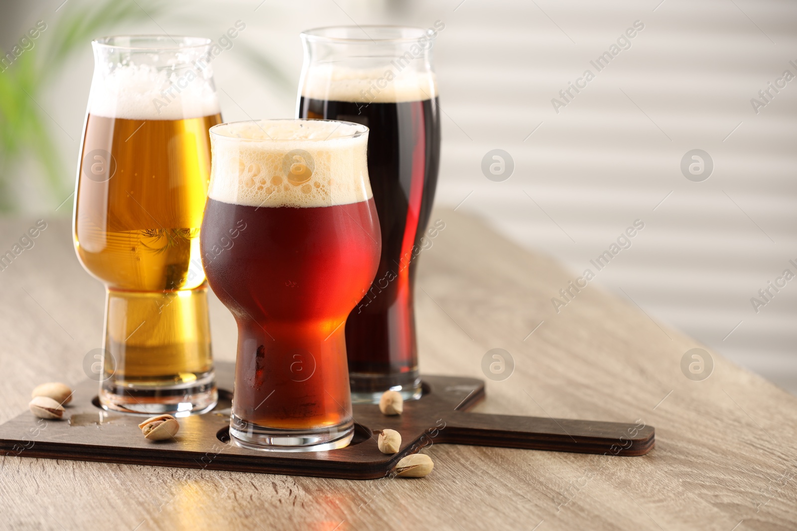 Photo of Glasses with different types of beer and pistachio nuts on wooden table indoors, space for text