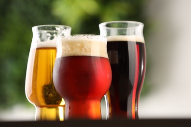 Photo of Glasses with different types of beer on table against blurred background, closeup