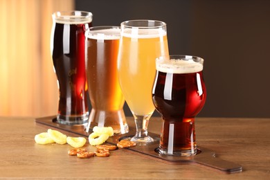 Photo of Glasses with different types of beer and snacks on wooden table indoors