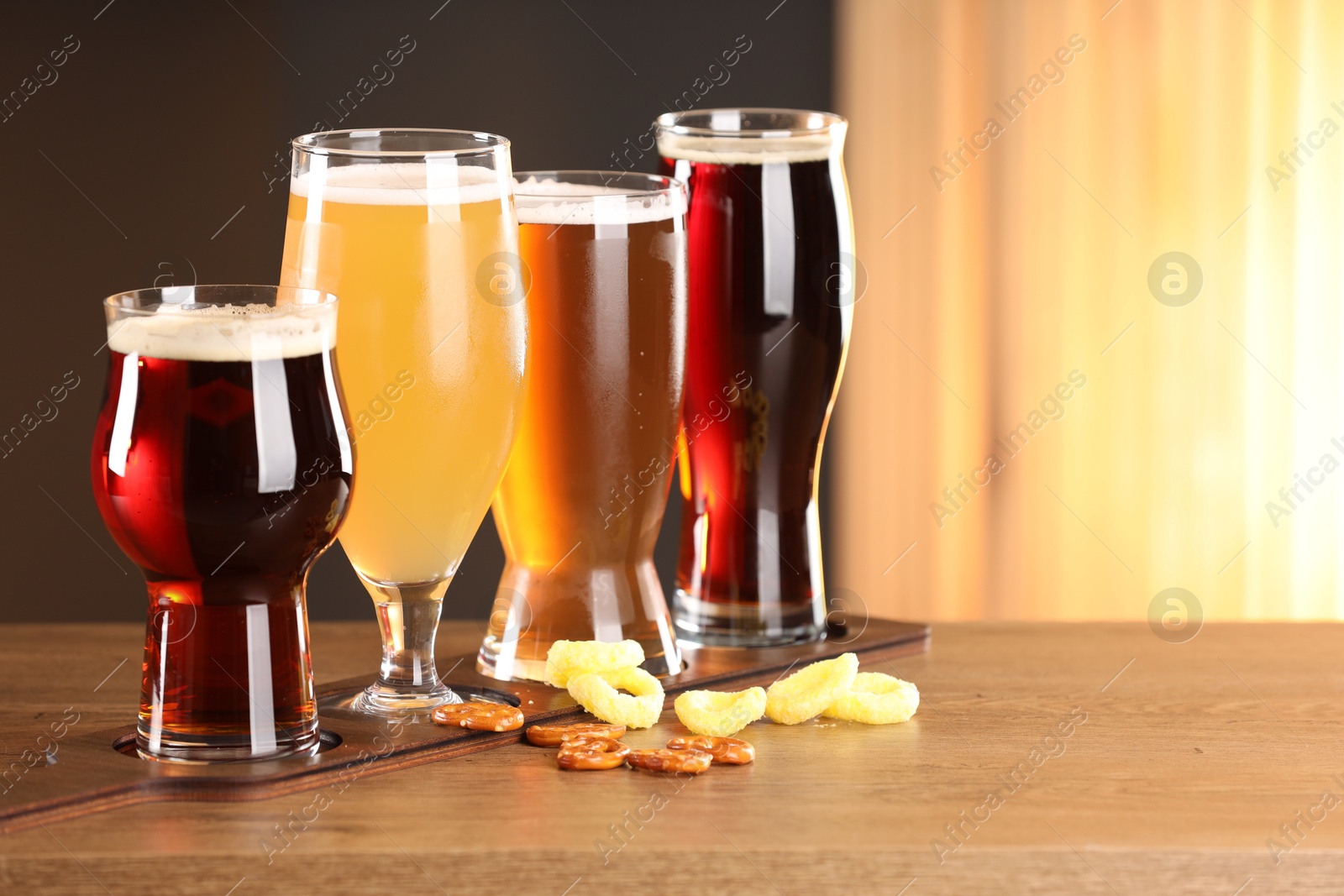 Photo of Glasses with different types of beer and snacks on wooden table indoors, space for text