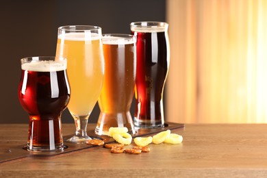 Photo of Glasses with different types of beer and snacks on wooden table indoors, space for text