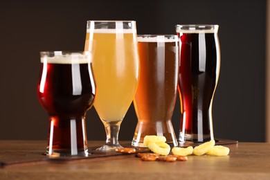 Photo of Glasses with different types of beer and snacks on wooden table indoors