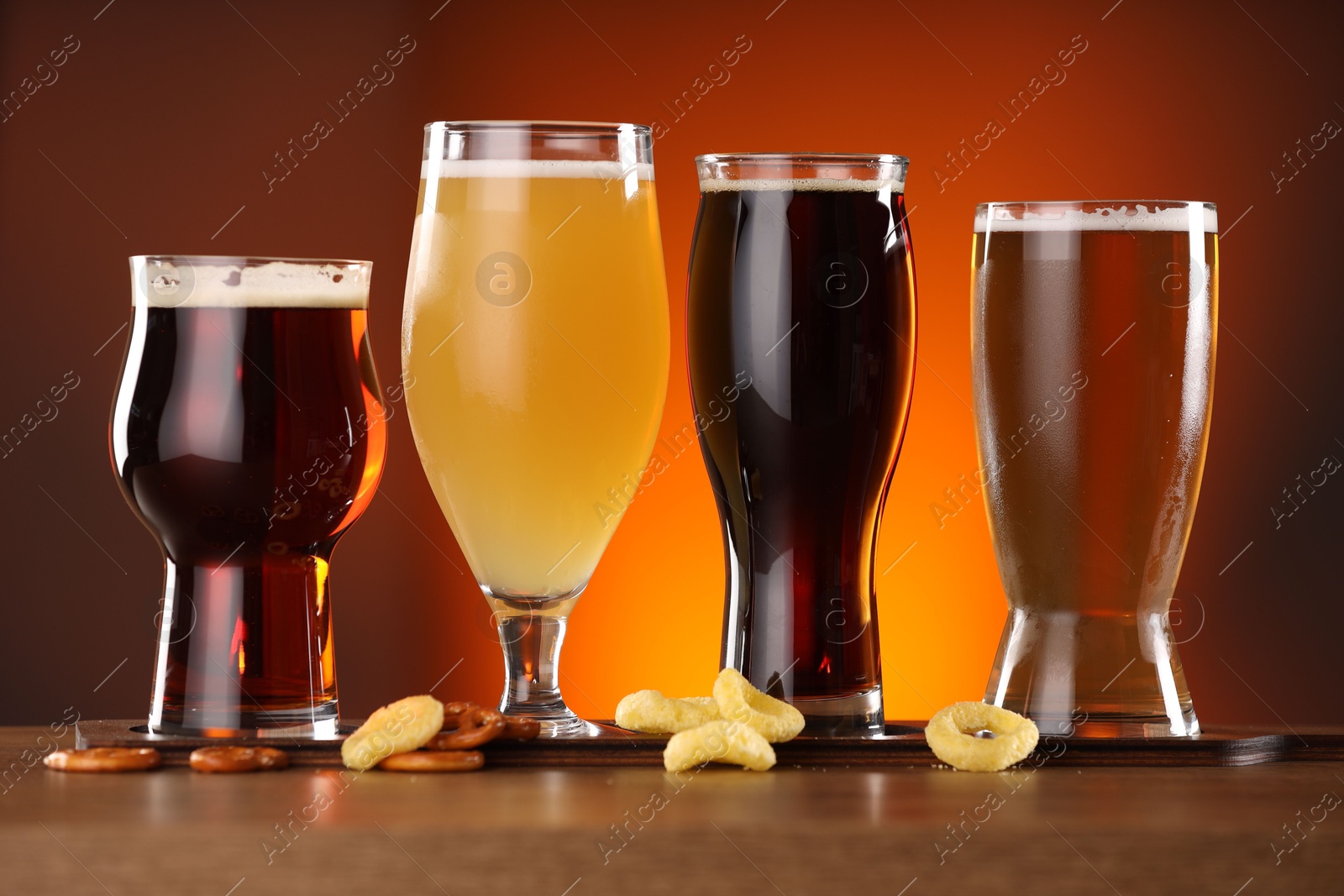 Photo of Glasses with different types of beer on wooden table against color background