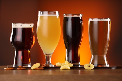 Photo of Glasses with different types of beer on wooden table against color background