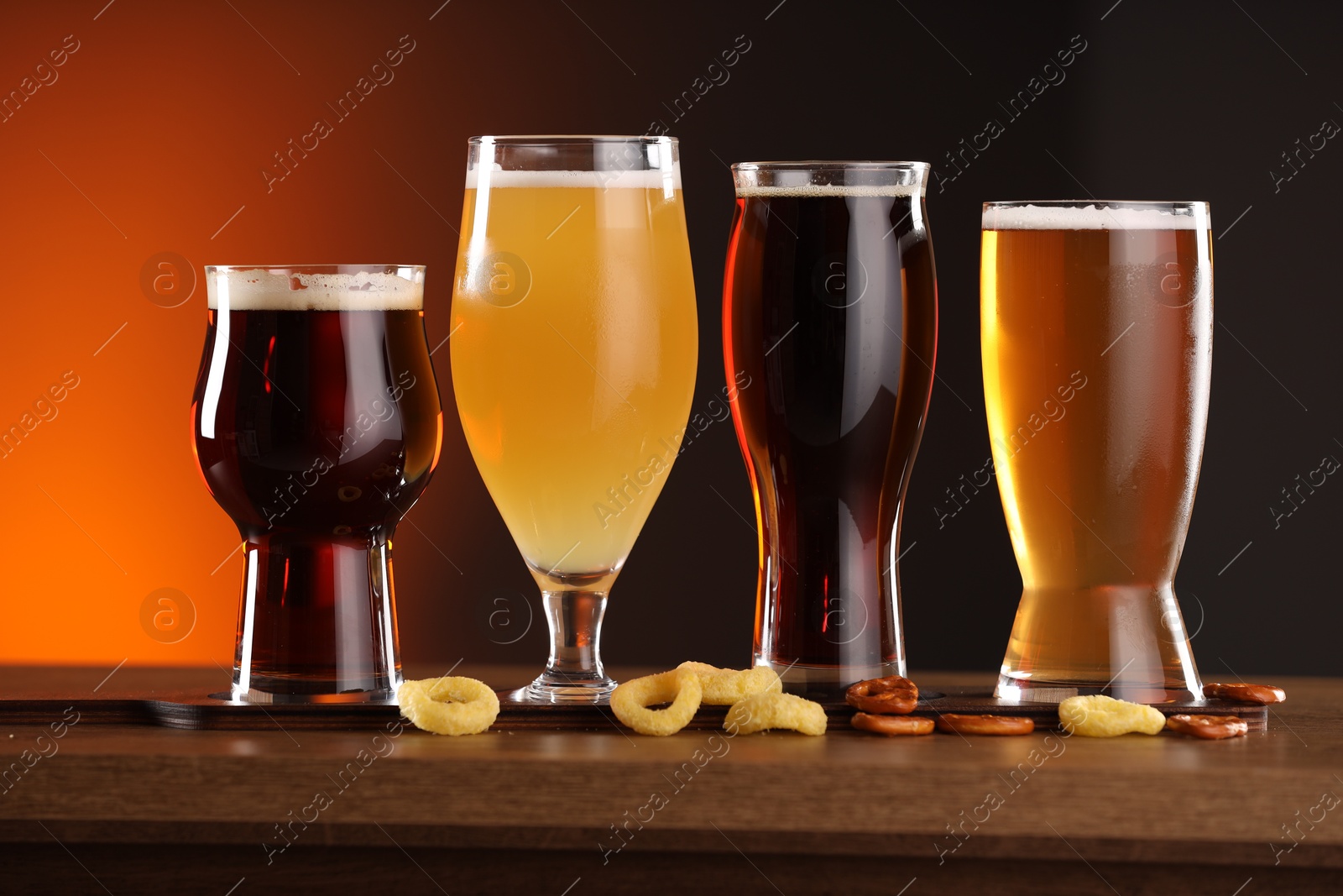 Photo of Glasses with different types of beer on wooden table against color background