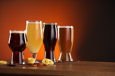 Photo of Glasses with different types of beer on wooden table against color background, space for text